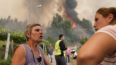 Dos vecinas hablan ante las llamas, que cada vez se acercan más a la población de Arbo (Pontevedra), donde se ha decretado "Situación 2"/EFE