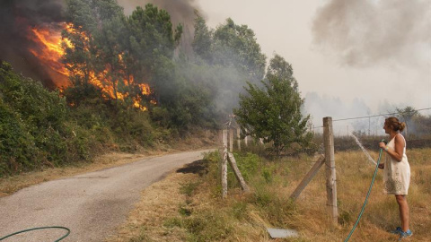 Una mujer observa como se acerca el fuego en Pontevedra con una manguera en la mano/EFE