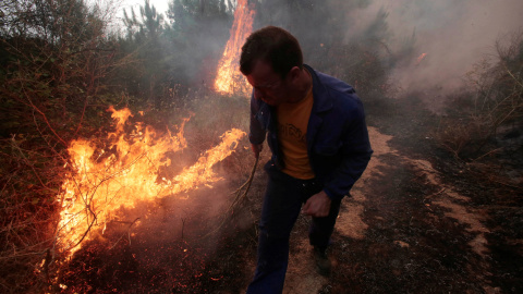 Han sido muchos voluntarios los que han ayudado a la extinción de los fuegos, en esta fotografía un hombre de Arbo, observa el fuego con una rama/REUTERS