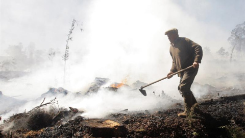 Un vecino ayuda a extinguir el indencio de San Juan de Fecha (Santiago de Compostela) de nivel 2, que ha obligado a desalojar varias poblaciones/EFE