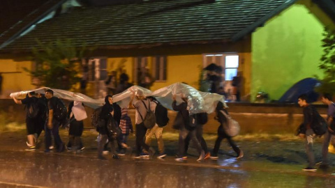 Los migrantes se protegen de la lluvia con un plástico mientras caminan para coger el tren en dirección a la frontera con Serbia, después de recibir el permiso para cruzar en Macedonia en la estación de tren en Gevgelija.-EFE Los migrantes se protegen de la lluvia con un plástico mientras caminan para coger el tren en dirección a la frontera con Serbia, después de recibir el permiso para cruzar en Macedonia en la estación de tren en Gevgelija.-EFE