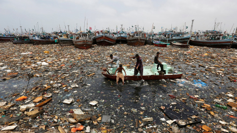 Niños a bordo de un barco abandonado recoge los objetos reciclables a través de aguas contaminadas en frente de barcos de pesca en el puerto de pescado en Karachi , Pakistán. REUTERS / Akhtar Soomro