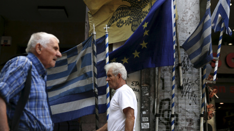 Dos hombres pasean en Atenas por delante de banderas griegas y europeas. /REUTERS Dos hombres pasean en Atenas por delante de banderas griegas y europeas. /REUTERS
