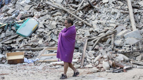 Un hombre que acaba de ser rescatado pasea entre los escombros de la que era su casa/REUTERS