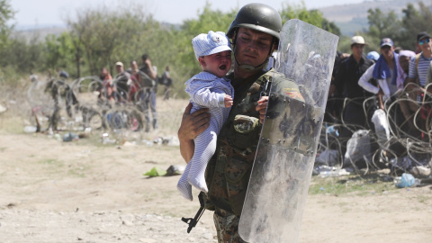 Un policía lleva un bebé a salvo mientras inmigrantes intentan cruzar la frontera de Macedonia y Grecia.  REUTERS/Ognen Teofilovski