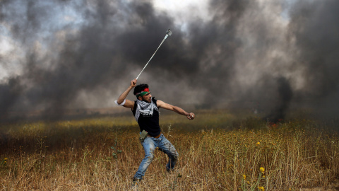 Un joven palestino arroja piedras a las tropas israelíes durante los enfrentamientos en una jornada protestas en las que ha colocado tiendas de campaña a lo largo de la frontera de Israel con Gaza, exigiendo el derecho a regresar a su tierr
