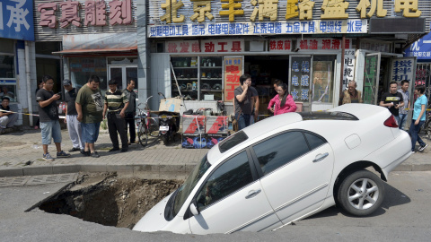 Transeúntes echan un vistazo a un coche que ha caído parcialmente en un socavón por una calle de Beijing. REUTERS
