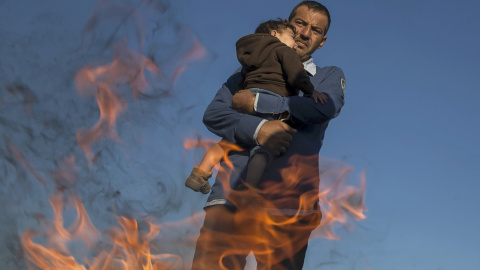 Un inmigrante con su hijo entrando en calor al lado de una fogata en un campamento improvisado en un punto de recogida en el pueblo de Röszke, Hungría, 8 de septiembre de 2015. REUTERS / Marko Djurica