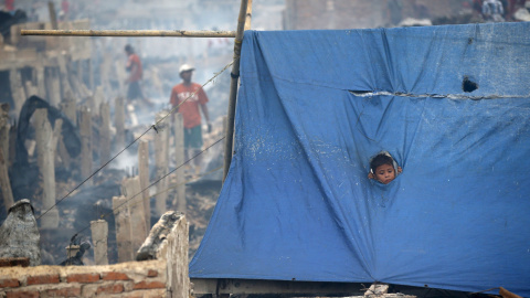 Un niño se asoma por un agujero en una lona en un refugio creado tras un incendio que destruyó cientos de viviendas en la zona Kapuk Raya del norte de Yakarta, 9 de septiembre de 2015. REUTERS / Darren Whiteside