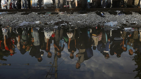 Refugiados sirios se reflejan en un charco mientras esperan en la frontera entre Grecia y Macedonia. REUTERS
