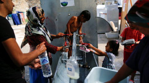 Anis, de cuatro años, lava su ropa en una fuente del campo de refugiados de Chios, en Grecia, junto a su madre/REUTERS