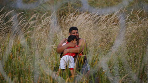 Un migrante que sostiene a su hijo en la parte serbia de la valla en Ásotthalom. REUTERS
