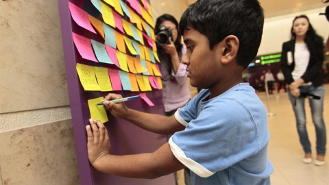 Un niño escribe un mensaje de apoyo a los pasajeros del vuelo QZ 8501 de AirAsia desaparecido, a las puertas de la zona de espera de familiares en el Aeropuerto Changi de Singapur. EFE