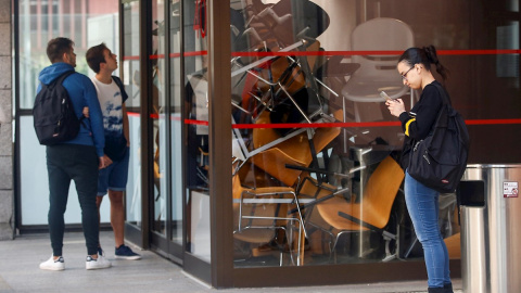 Varios estudiantes de la Universidad Pompeu Fabra (UPF) esperan este martes a las puertas de la facultad de Ciencias Sociales que ha despertado bloqueada con mesas y sillas por un centenar de universitarios que han pasado la noche en los ed