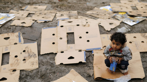 Un niño descalzo encima de un cartón con un paquete de galletas espera mientras los emigrantes esperan entrar en Croacia desde Berkasovo, Serbia. 28 de septiembre de 2015. REUTERS/Antonio Bronic