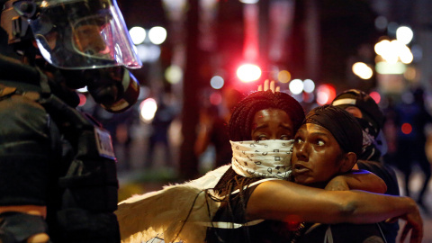 Dos mujeres se abrazan con la mirada asustada junto a un policía en Charlotte, Carolina del Norte durante la protesta. REUTERS / Jason Miczek