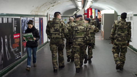 Una mujer lee laúlrima edición del semanario satírico 'Charlie Hebdo' mientras se cruza con un grupo de soldados franceses que patrulla en el interior de la estación de metro de Trocadero en París. EFE/Yoan Valat
