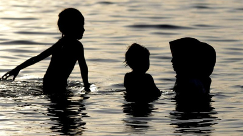 Una fotografía muestra las siluetas de una mujer musulmana que lleva la vestimenta islámica en el agua con dos niños en la playa en Ule Lhuee, Banda Aceh, Indonesia. EFE