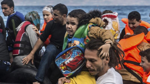Un voluntario ayuda a un niño refugiado a su llegada a la costa tras una dura travesía en lancha neumática, en la isla de Lesbos (Grecia). Alrededor de 100.000 refugiados y migrantes llegaron a las islas griegas durante el mes de agosto, se