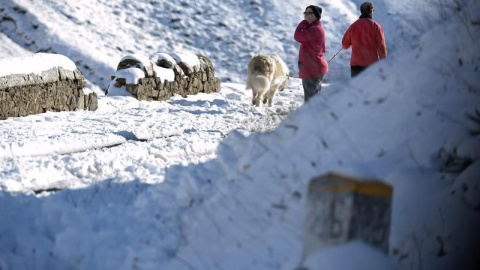 Dos personas pasean por la carretera comarcal CA-643 en la subida al puerto de Lunada por la red secundaria donde es obligatorio el uso de cadenas y donde esta activada la alerta por nevadas. EFE/Pedro Puente Hoyos