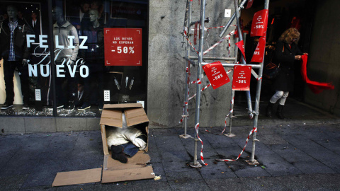 Una mujer sale de una tienda en rebajas mientras un hombre duerme en unas cajas en la calle en Madrid. REUTERS