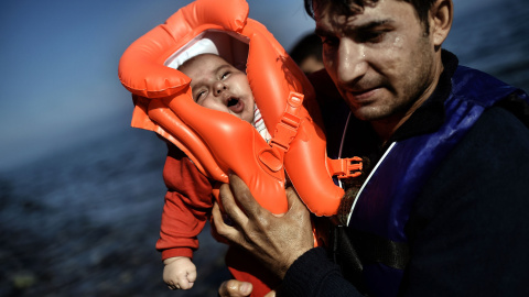 Un emigrante sujeta un bebé mientras refugiados y emigrantes llegan a la isla griega de Lesbos después de cruzar el mar Egeo desde Turquía el 5 de octubre de 2015. AFP / ARIS MESSINIS