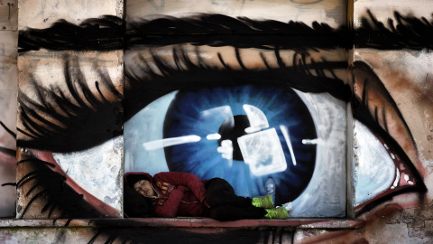 Una mujer emigrante duerme debajo de una pintada de un ojo en el puerto de Mitilene, en la isla griega de Lesbos, el 6 de octubre de 2015. AFP/ARIS MESSINIS
