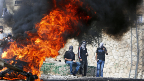 Jóvenes palestinos  lanzando piedras de pie junto a un fuego durante los enfrentamientos con la policía israelí en el este árabe de Jerusalén