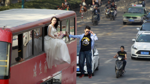 El mago Lei Xin es fotografiado colgado de un autobús , al lado de una mujer vestida de novia, mientras actúan en una calle de Zhengzhou, provincia de Henan, China. REUTERS / Stringer,