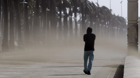 Un hombre camina entre la vetisca de arena por el paseo maritimo de Almeria, provincia que se encuentra en alerta naranja por fuertes vientos. EFE / Carlos Barba