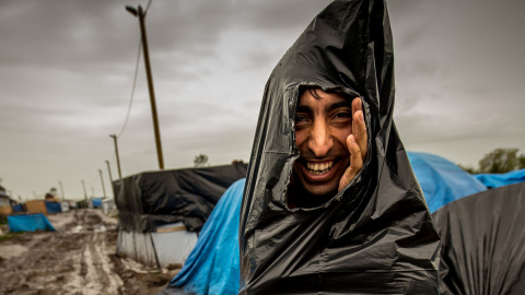 Un inmigrante se protege de la lluvia con una bolsa de basura en el campamento de inmigrantes en Calais, donde miles viven con la esperanza de cruzar a Reino Unido. AFP PHOTO / PHILIPPE HUGUEN