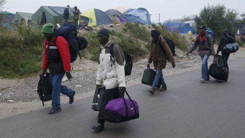 Un grupo de refugiados caminan con sus pertenencias junto a las tiendas de campaña de la 'Jungla' de Calais  durante el desmantelamiento de esta. REUTERS/Pascal Rossignol