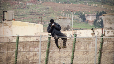 Un immigrante africano come un sándwich lanzado por agentes de la Guardia Civil, mientras permanece sentado en lo alto de la valla de Melilla. /JESÚS BLASCO DE AVELLANEDA (REUTERS)