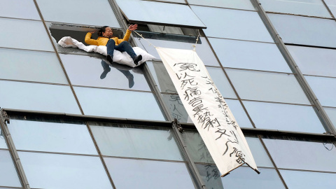 Una mujer se sienta en el borde de una ventana que previamente ha roto, al lado de una bandera anunciando su intención de suicidarse por una disputa financiera con en funcionario del gobierno local, según los medios. La mujer finalmente se 