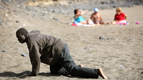 Un inmigrante exhausto llega a la  playa de Fuerteventura, en Canarias, ante la mirada de los turistas (5 de mayo de 2006). REUTERS / Juan Medina