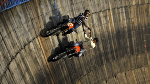 Acróbatas montan en sus motocicletas en las paredes del pozo de la muerte en una feria en las afueras de Bangalore, en la India. REUTERS