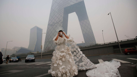 Una mujer posa con un vestido de novia confeccionado con 999 mascarillas para su 'performance' artística 'Cásate con el azul del cielo', ante la sede de la Televisión Central China (CCTV) en un día brumoso en Pekín. /KIM KYUNG-HOON (REUTERS