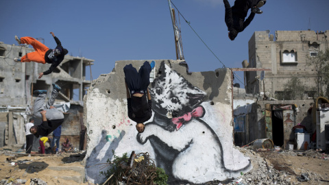Jovenes palestinos hacen parkour junto a una pintada del artista británico Banksy. / AFP