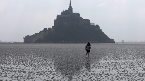Una mujer camina en la arena durante la marea baja cerca de la abadía del Mont Saint-Michel, en Normandía. REUTERS / Pascal Rossignol