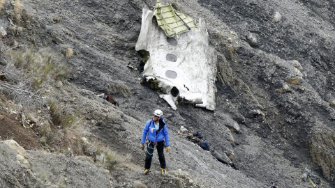 Un miembro de los servicios de rescate camina al lado del mayor un tramo de fuselaje del avión siniestrado, en el que se aprecian tres ventanillas, entre millones de fragmentos del aparato esparcidas por una amplia área de alta montaña en l