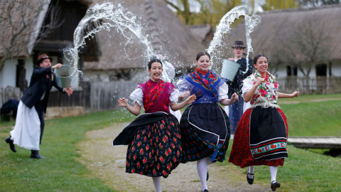 Tres mujeres corren mientras los hombres les lanzan agua, durante las celebraciones tradicionales de Pascua en Szenna (Hungría). / LASZLO BALOGH (REUTERS)