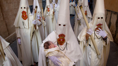Un miembro de la hermandad del Cristo de la Sangre, lleva a un bebé durante una procesión de Pascua, en Palma de Mallorca. /JAIME REINA (AFP)
