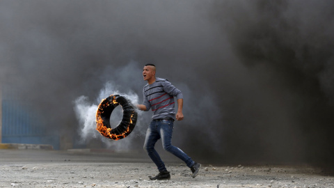 Un manifestante palestino, con un neumático en llamas durante un enfrentamiento con tropas israelíes, en protesta por los asentamientos judíos, en Jalazoun, cerca de la ciudad cisjordana de Ramala. /MOHAMAD TOROKMAN (REUTERS)
