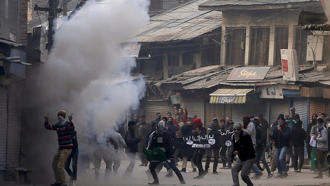 Manifestantes de Cachemira sostienen una bandera similar a la bandera utilizada por el Estado Islámico en medio del humo del gas lacrimógeno lanzado por la policía de la India durante una protesta en Srinagar. Los manifestantes exigían la l
