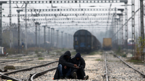 Dos hombres se sientan en las vías del tren mientras emigrantes y refugiados esperan para cruzar la frontera entre Grecia y Macedonia cerca Idomeni el 25 de noviembre de 2015.  AFP / SAKIS MITROLIDIS