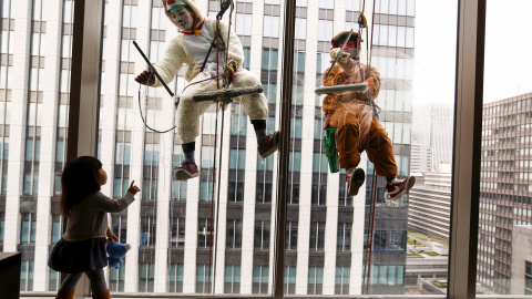 Una niña observa a los limpia cristales de un hotel en Tokio que van disfrazados de una obeja y un mono./ REUTERS/Thomas Peter