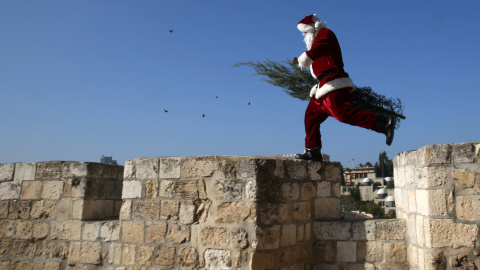 Un palestino cristiano vestido de Papá Noel camina con un árbol de Navidad a lo largo de los muros viejos de la ciudad de Jerusalén mientras los cristianos de todo el mundo se preparan para celebrar la Navidad. AFP/GALI Tibbon