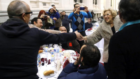 La alcaldesa de Madrid, Manuela Carmena (d), saluda a algunas de las 200 personas sin hogar que esta noche cenan en el Palacio de Cibeles, organizadas por la Fundación Mensajeros de la Paz que preside el padre Ángel en colaboración con el A