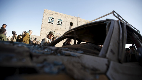 La gente se reúne alrededor de un coche dañado por un ataque aéreo saudita llevado a cabo a las afueras de la capital de Yemen, Saná, 29 de diciembre de 2015. REUTERS / Khaled Abdullah