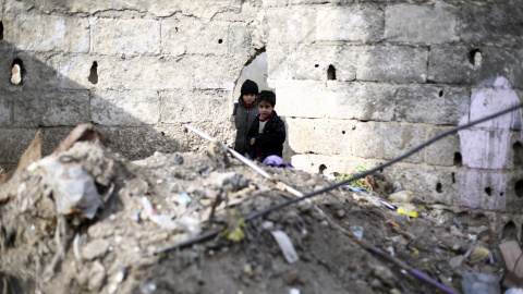 Dos niños miran a través de un agujero en un muro de una calle de Douma, afueras de Damasco, Siria, el 29 de diciembre del 2015. Más de cuatrocientas personas, entre heridos, rebeldes y civiles, fueron evacuadas ayer de varias ciudades ased